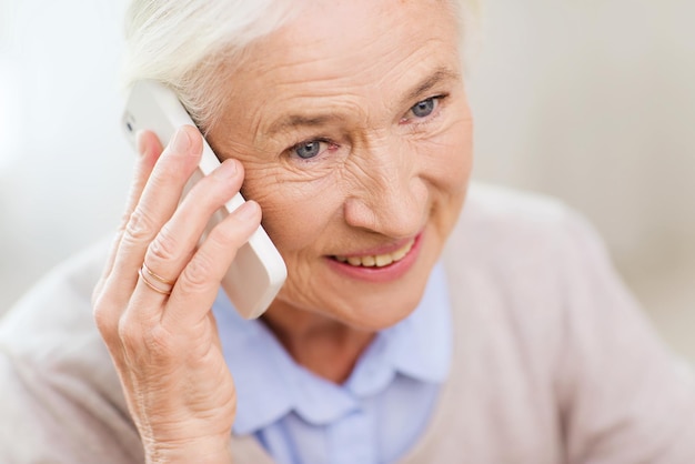 technology, communication age and people concept - happy senior woman with smartphone calling at home