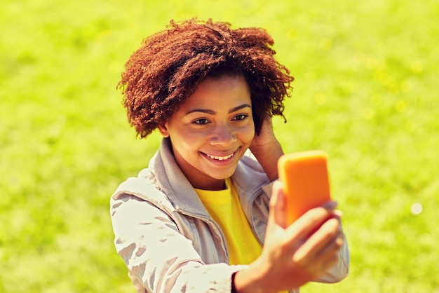 технологии, общение и концепция людей - счастливая африканская женщина делает селфи со смартфоном в летнем парке