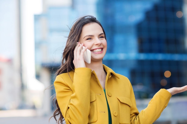 technology, communication and people concept - smiling young woman or girl calling on smartphone on city street