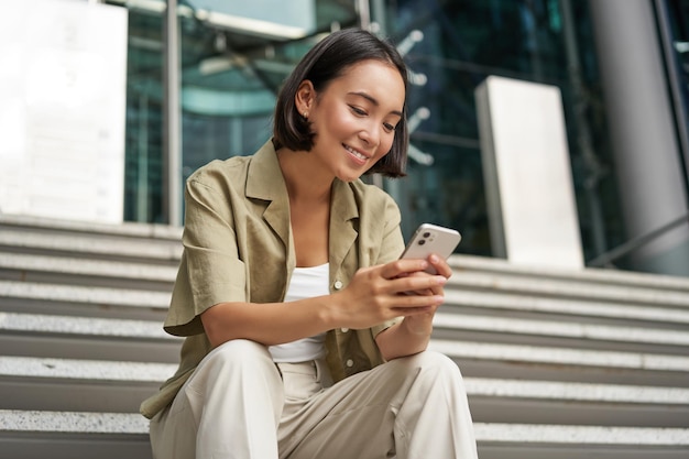 Photo technology and communication young smiling girl asian woman sits with smartphone reads message with