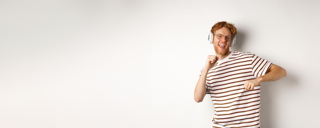 Technology concept happy redhead man listening music in headphones and dancing cheerful standing in