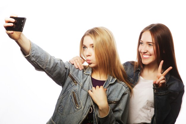 Technology, friendship and people concept - two smiling teenagers taking picture with smartphone camera