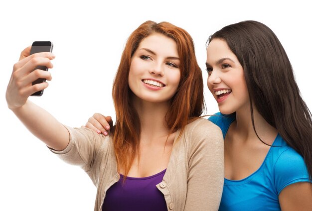 テクノロジー、友情、人々のコンセプト-スマートフォンのカメラで写真を撮る2人の笑顔のティーンエイジャー