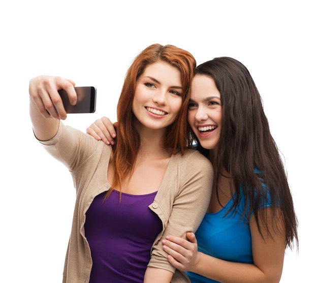 technology, friendship and people concept - two smiling teenagers taking picture with smartphone camera