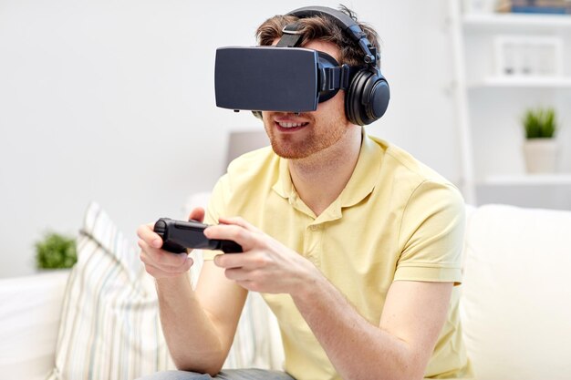 technology, gaming, entertainment and people concept - happy young man with virtual reality headset or 3d glasses playing video game with controller gamepad at home