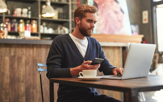 Technology gives him the freedom to work anywhere Shot of a young man using a laptop and phone in a cafe