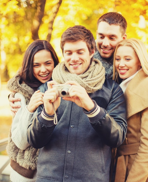 technology, holidays, travel, happy people concept - group of friends or couples having fun with photo camera in autumn park