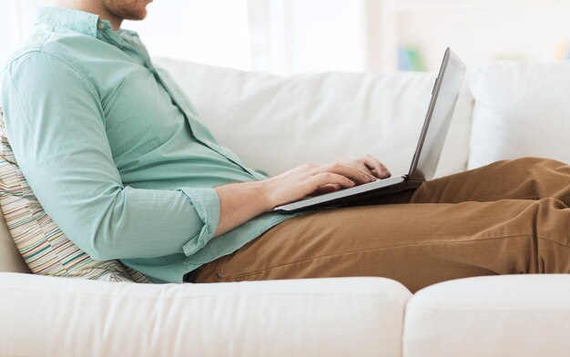 technology, home and lifestyle concept - close up of man working with laptop computer and sitting on sofa at home