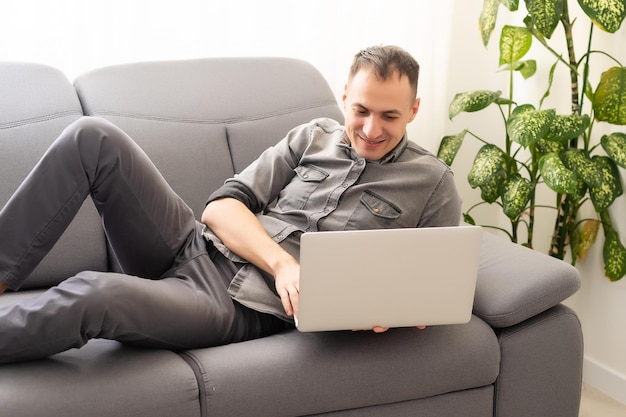 technology, home and lifestyle concept - close up of man working with laptop computer and sitting on sofa at home.