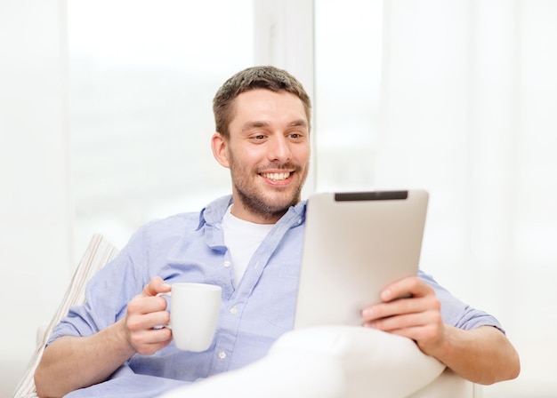 Concetto di tecnologia, casa e stile di vita - uomo sorridente che lavora con computer tablet pc e tazza di caffè a casa