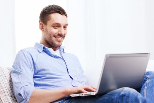 технологии, дом, люди и концепция образа жизни - улыбающийся мужчина, работающий с ноутбуком дома