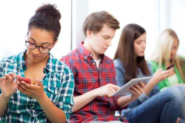 Photo technology and internet concept - students looking into phones and tablet pc at school