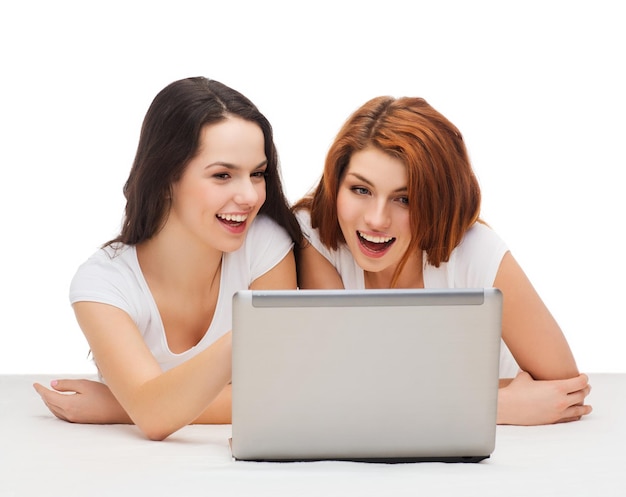 technology, internet and entertainment concept - two smiling teenage girls in white t-shirts with laptop computer