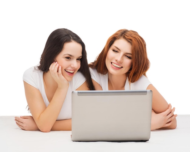 technology, internet and entertainment concept - two smiling teenage girls in white t-shirts with laptop computer