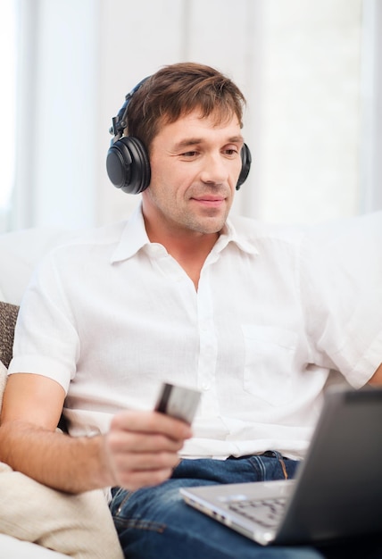 기술, 레저, 라이프스타일 개념 - 헤드폰과 신용카드로 집에서 음악을 듣는 행복한 남자