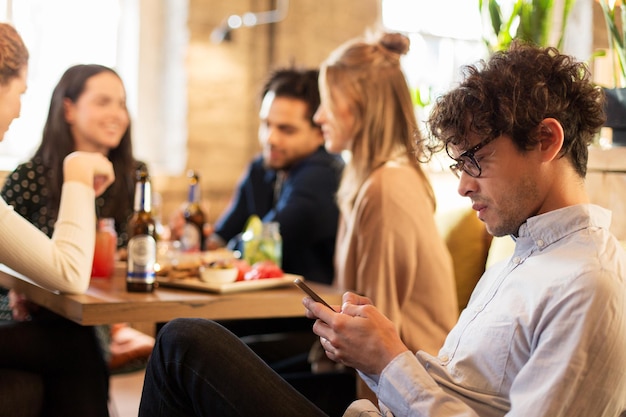 テクノロジーライフスタイル休日人々コンセプト - スマートフォンとレストランの友達を持つ男性
