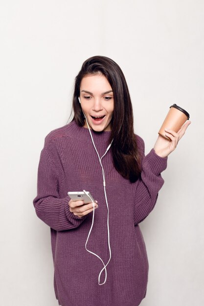 기술, 생활 방식, 인터넷 중독, 그리고 사람들의 개념 - 스마트 폰을 가진 젊고 아름다운 여성. 휴대 전화를 보고 행복 하 고 웃는 매력적인 여자. 배경에 회색 벽입니다.