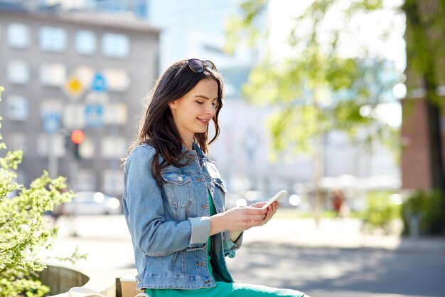 技術、ライフ スタイル、人々 のコンセプト - 笑顔の若い女性や 10 代の少女の街でスマート フォンのテキスト メッセージ