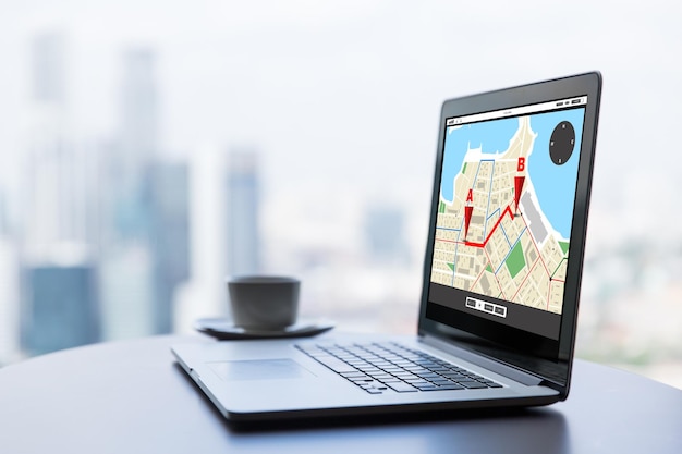 technology, location, navigation, business and modern life concept- close up of open laptop computer with gps navigator map on screen and coffee cup on table at office or hotel room