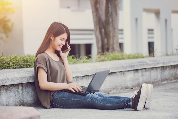 Технологии современного образа жизни, азиатские милые подростки, звонящие со смартфона и использующие ноутбук, наслаждаются счастьем и улыбкой в кампусе