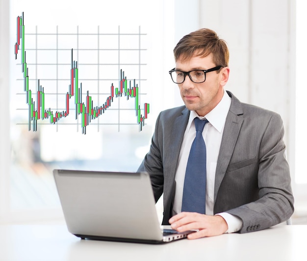 technology, money, business and office concept - handsome businessman in black eyeglasses with laptop computer and forex chart