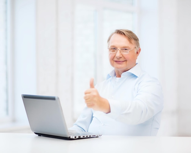 technology, oldness and lifestyle concept - old man in eyeglasses with laptop computer at home showing thumbs up