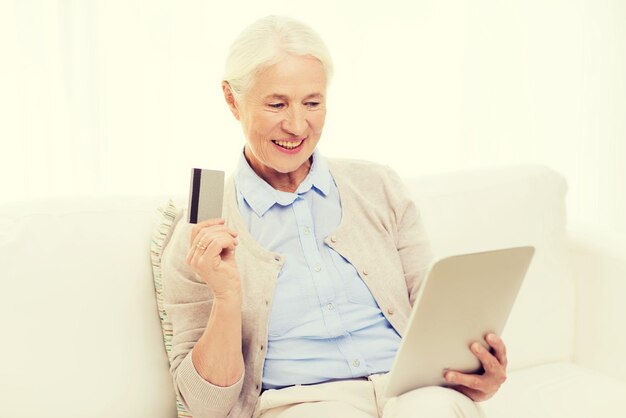 technology, online shopping, age and people concept - happy senior woman with tablet pc computer and credit or bank card at home