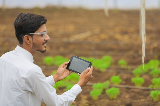 Concetto di tecnologia e persone, giovane agronomo indiano utilizzando tablet o smartphone in serra