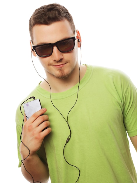 Concetto di tecnologia e persone - giovane uomo che indossa una maglietta verde ascolta musica e utilizza smartphone, isolato su bianco