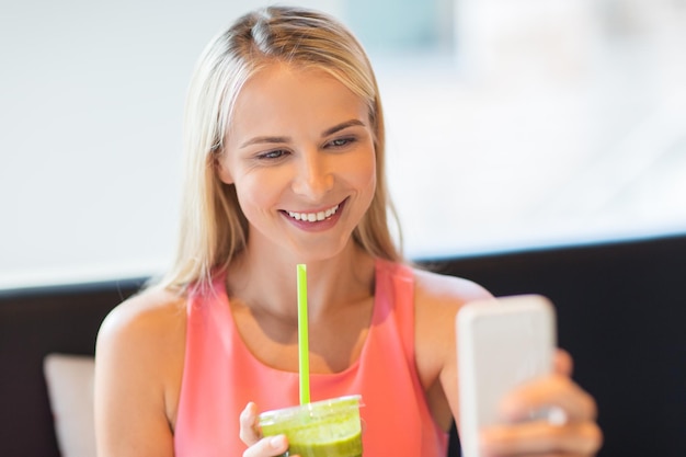 technology, people and leisure concept - happy woman with smartphone and smoothie drink or vegetarian shake taking selfie at restaurant