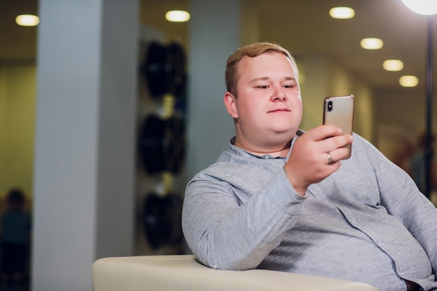 Concetto di tecnologia, della gente, di stile di vita e di comunicazione - uomo felice con il telefono che ha casa di video chiamata e che mostra i pollici su che si siedono sul sofà in ufficio