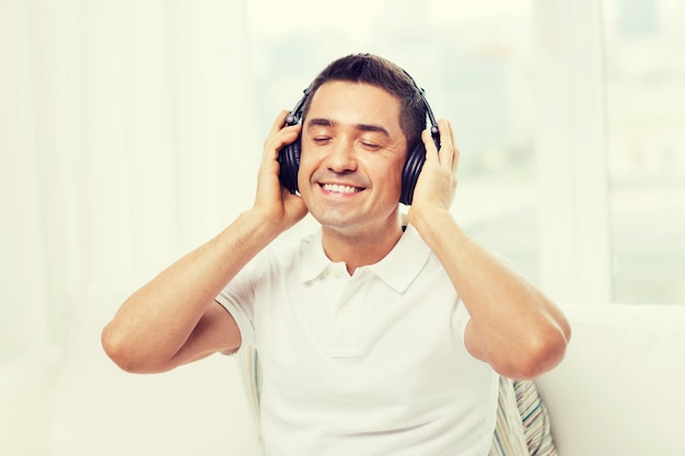 テクノロジー、人、ライフスタイルのコンセプト-自宅で音楽を聴くヘッドフォンで幸せな男