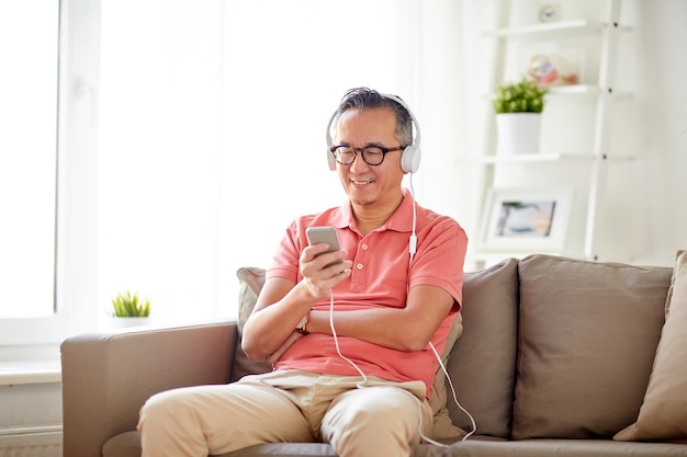 기술, 사람, 라이프스타일 개념 - 스마트폰과 헤드폰을 끼고 집에서 음악을 듣는 행복한 남자