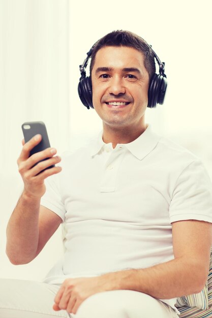 technology, people, lifestyle and distance learning concept - happy man with smartphone and headphones listening to music at home