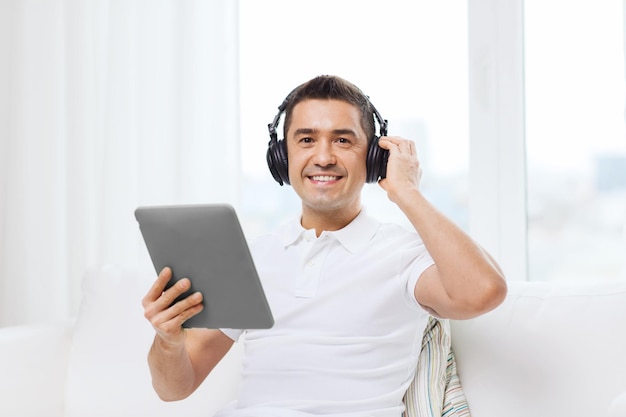 technology, people, lifestyle and distance learning concept - happy man with tablet pc computer and headphones listening to music at home