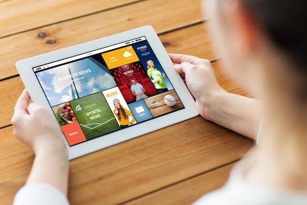 technology, people and mass media concept - close up of woman with news on tablet pc computer screen on wooden table