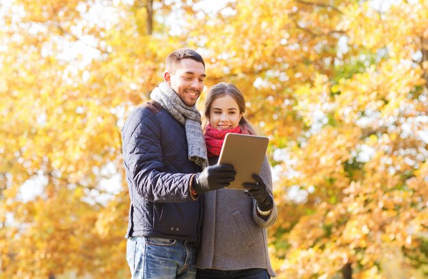 technology, relationship, family and people concept - smiling couple with tablet pc computer in autumn park