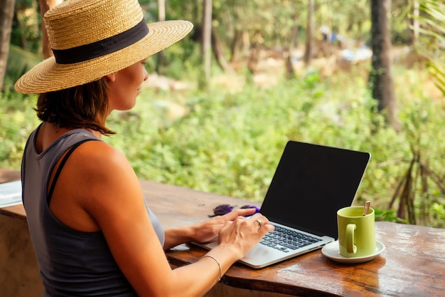 Technology and travel working outdoors freelance concept pretty\
young woman in hat using laptop in cafe on tropical beachhooray\
victory success and successful deal concept promotion at work