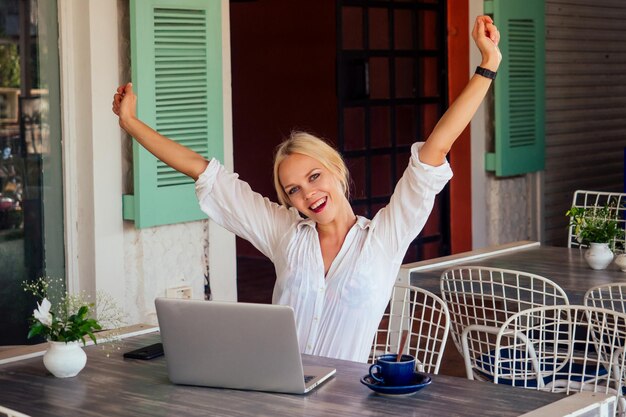 Technology and travel Working outdoors Freelance concept Pretty young woman using laptop in cafe on tropical beachHooray victory success and successful deal concept promotion at work