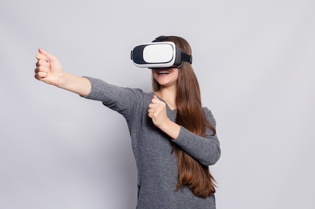 Technology, virtual reality, entertainment and people concept - happy young woman with virtual reality headset or 3d glasses. Woman with virtual reality goggles. Studio shot, gray background