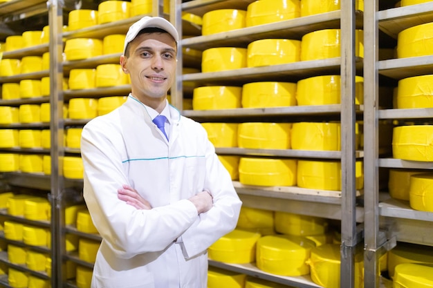 Technoloog in een witte jas is in het pakhuis van kaas in de winkel voor de productie van boter en kaas Het productieproces in de fabriek van zuivelproducten Rekken met kaas