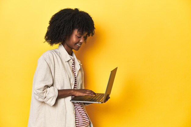 Techsavvy AfricanAmerican teenage girl with laptop on yellow studio background