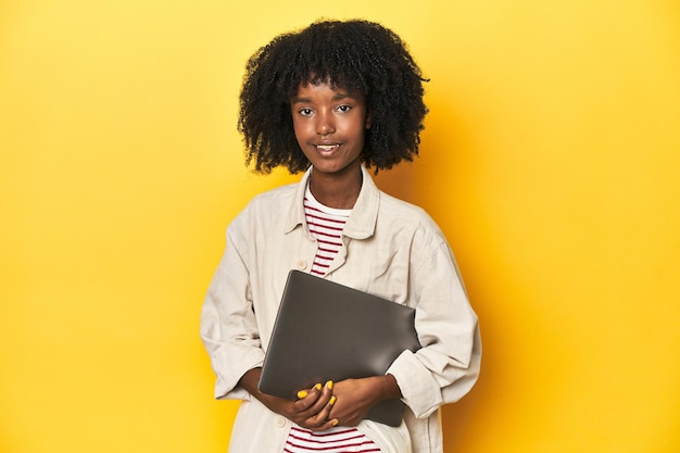 Techsavvy Afro-Amerikaanse tienermeisje met laptop op gele studio achtergrond