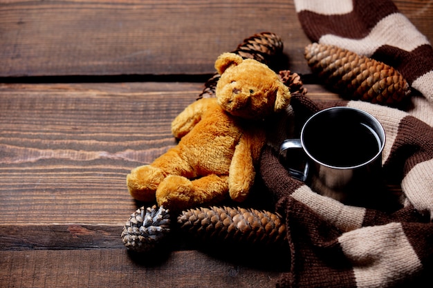 Teddy bear and cup of coffee with scarf on wooden table