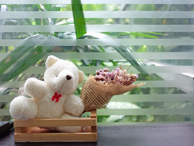 Teddy bear doll with dry grass flower on table near glass windows.