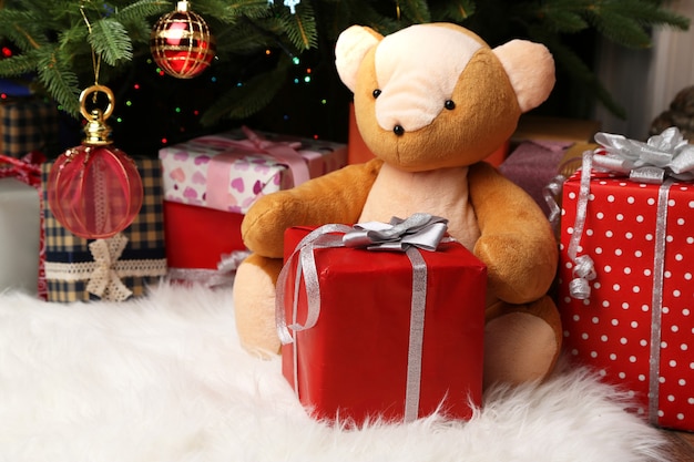 Teddy bear and gift boxes near Christmas tree, close-up