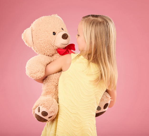 Foto orsacchiotto felice e schiena di un bambino in studio con un grande giocattolo soffice e carino come regalo o regalo adorabile bambina innocente e giovane che abbraccia il suo orsacchiotto con cura e felicità su sfondo rosa