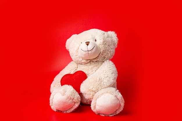 Teddy bear holding a heart isolated on red