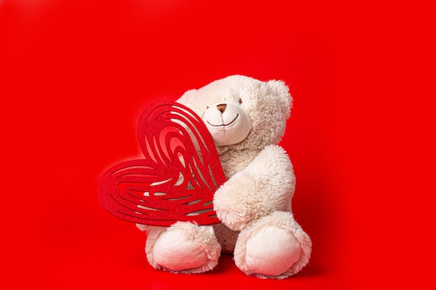 Teddy bear holding a heart isolated on red