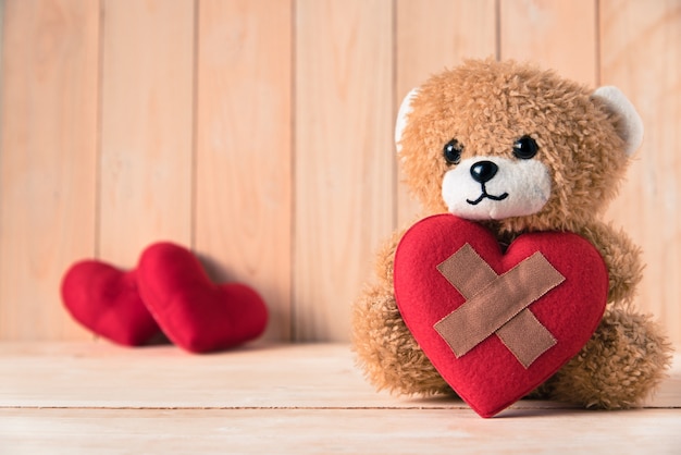 teddy bear holding wound heart with couple red heart background